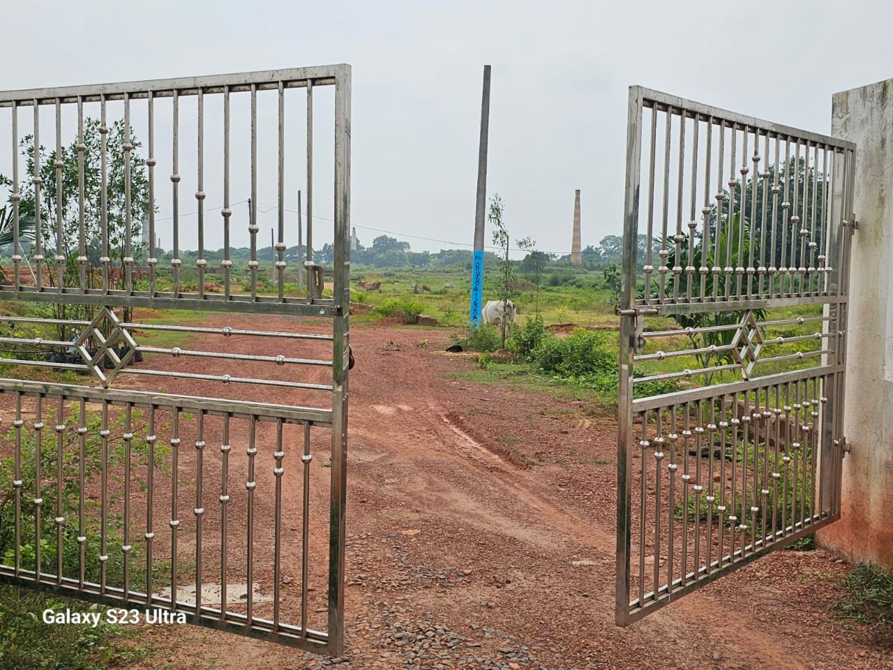 Steel entrance gate to the Mohan Dham gated township with brick-kiln horizon