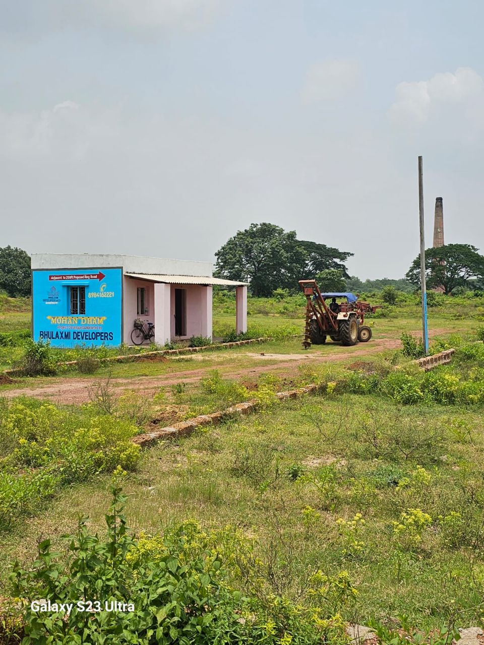 Mohan Dham site office at Pratap Nagari with project signage and tractor on plot
